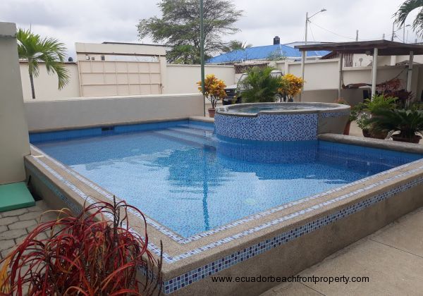 A good sized pool with jacuzzi set amongst some plants beside the gardens of the patio. 