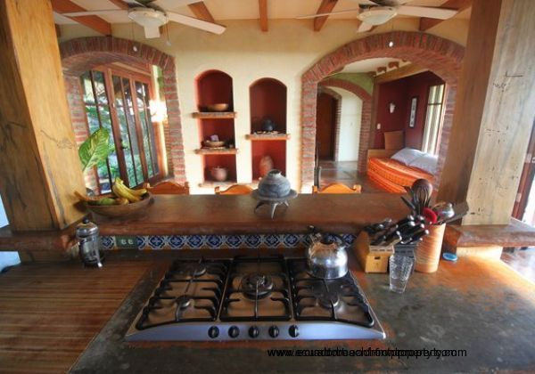 Kitchen opens to a living area with recessed shelving, broad archways, and large picture windows to maximizing views towards tropical gardens and the beach